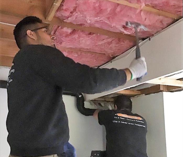 2 men with servpro shirts on standing on ladders removing insulation from ceiling