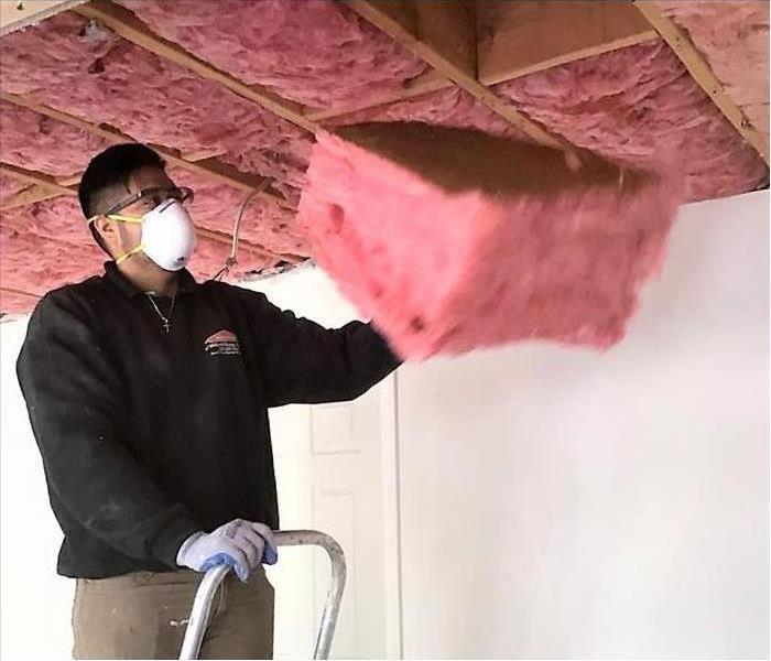 servpro technician removing wet insulation from a ceiling