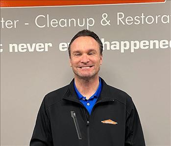 smiling man with brown hair and a black Servpro jacket on